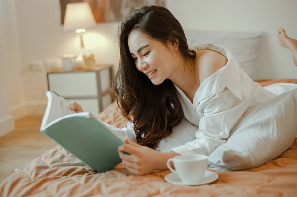 Jonge vrouw azië wonen thuis ontspannen en het lezen van een boek in de slaapkamer op vakantie. Aziatisch, aziatisch, ontspannen, alleen, technologie, lifestyle concept. - Foto, afbeelding