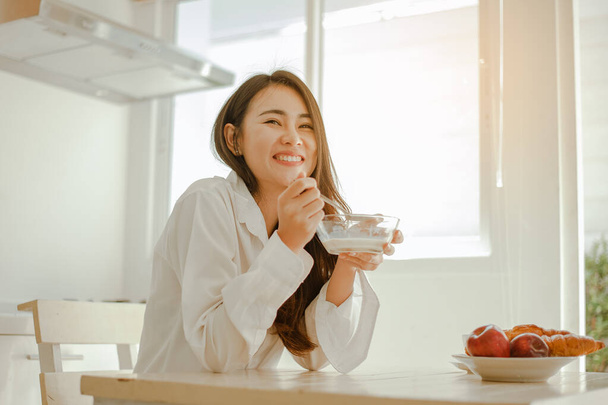 Young woman asia wake up refreshed in the morning and relaxing eat coffee, cornflakes, bread and apple for breakfast at house on holiday. Asian, asia, relax, breakfast, refresh, lifestyle concept. - Photo, Image