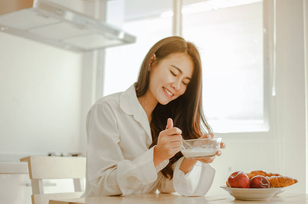 Young woman asia wake up refreshed in the morning and relaxing eat coffee, cornflakes, bread and apple for breakfast at house on holiday. Asian, asia, relax, breakfast, refresh, lifestyle concept. - Valokuva, kuva