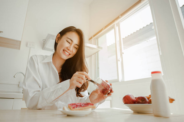 Young woman asia wake up refreshed in the morning and relaxing eat coffee, cornflakes, bread and apple for breakfast at house on holiday. Asian, asia, relax, breakfast, refresh, lifestyle concept. - 写真・画像