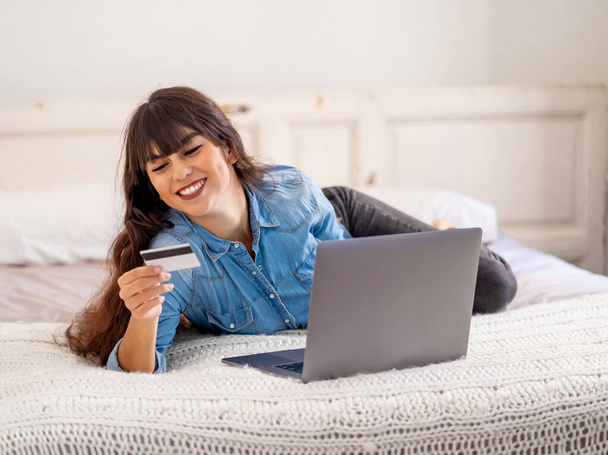 COVID-19 Ausbruch. Shutdown und Online-Shopping. Attraktive junge Frau mit Kreditkarte am Laptop, die zu Hause während der Coronavirus-Sperre und sozialer Distanzierung Lebensmittel im Internet kauft. - Foto, Bild