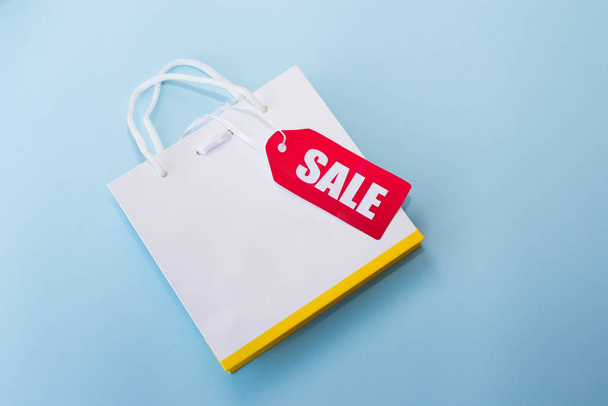 shopping bag bianca con etichetta rossa in vendita su sfondo blu. copia spazio
 - Foto, immagini