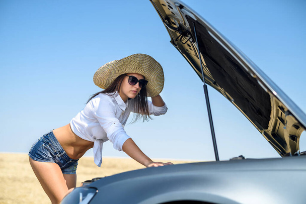 Stresli genç bir kadın arabasının motoruna bakıyor. Yolculuk sorunları. Arabanın tamire ihtiyacı var.. - Fotoğraf, Görsel