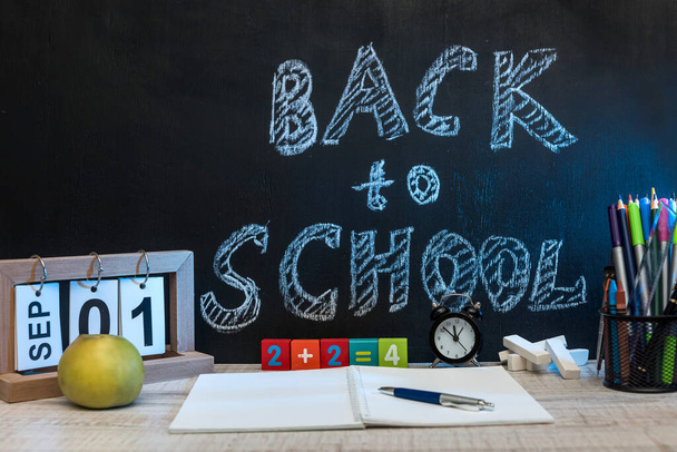 Zátiší s hodinami, psacím materiálem, knihou a jablkem proti tabuli s textem "zpět do školy"  . - Fotografie, Obrázek