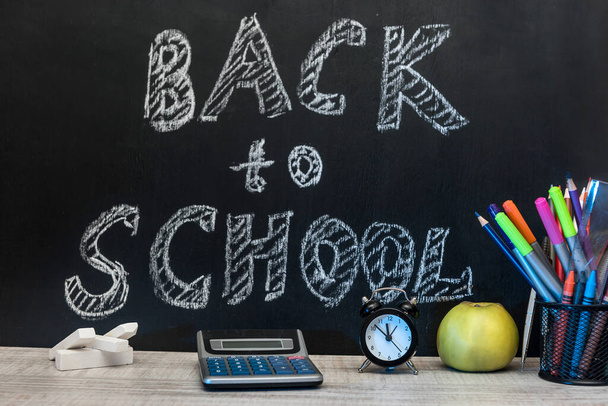 Saati, yazma materyalleri, bir kitap ve karatahtaya karşı bir elma "okula geri dön" yazılı."  . - Fotoğraf, Görsel