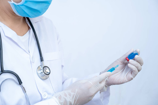 La main du médecin tient un tube de sérum bleu et une seringue
. - Photo, image
