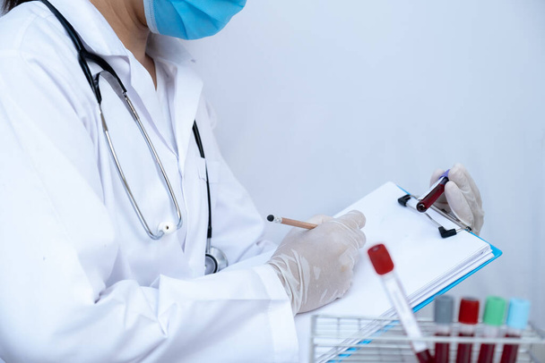 Médico de la mano sosteniendo el tubo sanguíneo y registrando los resultados del análisis de sangre
. - Foto, Imagen