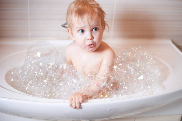 Funny child playing with water and foam in a bathroom. little boy bathes. - Fotó, kép