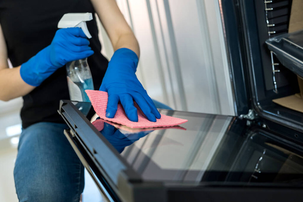 young woman cleaning the oven with rubber gloves and rag. cleaning concept - Foto, afbeelding