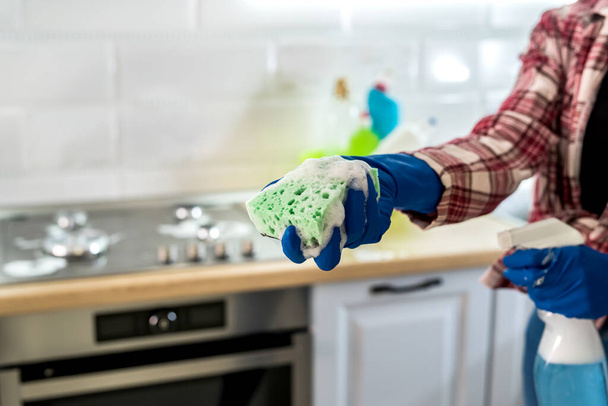 νεαρή γυναίκα καθαρισμού σε ελαστικά γάντια και σφουγγάρι στην κουζίνα στο σπίτι. - Φωτογραφία, εικόνα