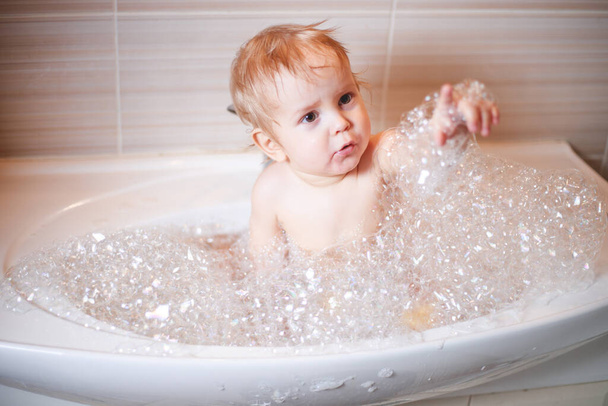 Happy laughing Infant baby toddler taking a bath playing with foam bubbles. Bathing and washing of little kid. Children care and hygiene concept. - Fotó, kép