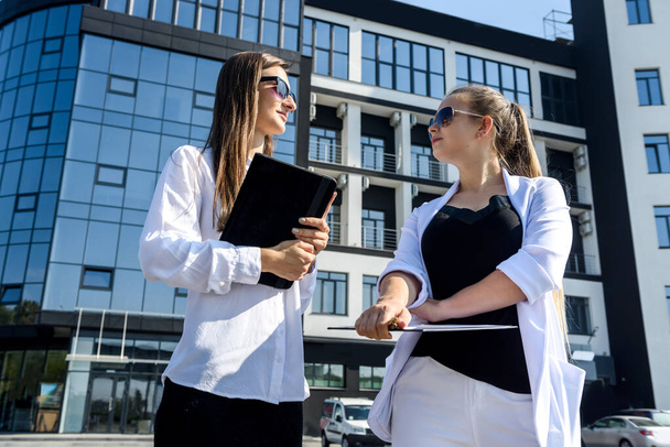 Two businesswoman holding tablets and talking opposite office building - Photo, Image