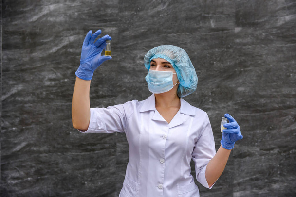 Chemisch onderzoek van de reageerbuis met stof. Ze draagt een beschermend uniform over grijze abstracte grijze achtergrond. - Foto, afbeelding