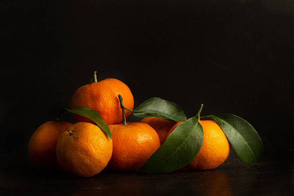 Haufen Mandarinen mit grünen Blättern auf dunklem Hintergrund - Foto, Bild
