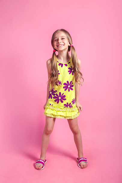 Cheerful little child girl in summer dress posing on a colored pink background. Vacation concept - Foto, imagen