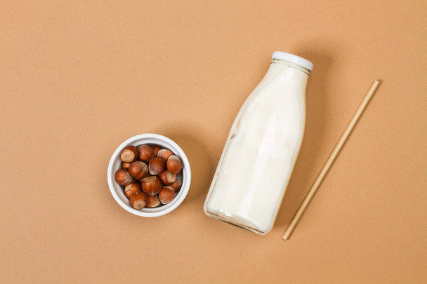 Uma garrafa de leite com avelãs em uma tigela branca em um fundo marrom em uma vista superior
 - Foto, Imagem
