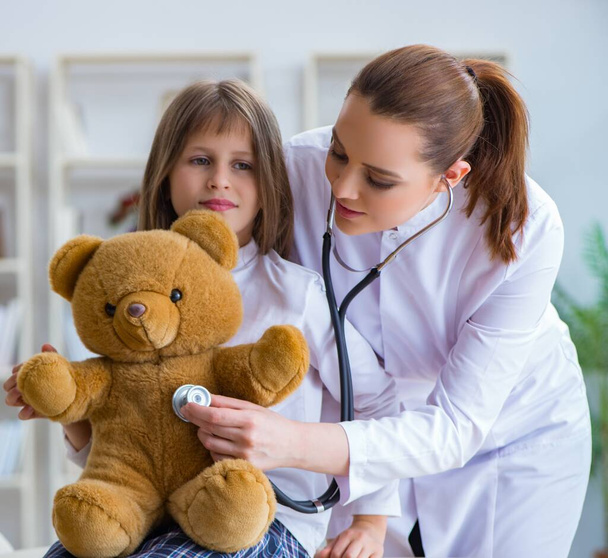 Жінка-лікар вивчає маленьку милу дівчинку з іграшковим ведмедем
 - Фото, зображення