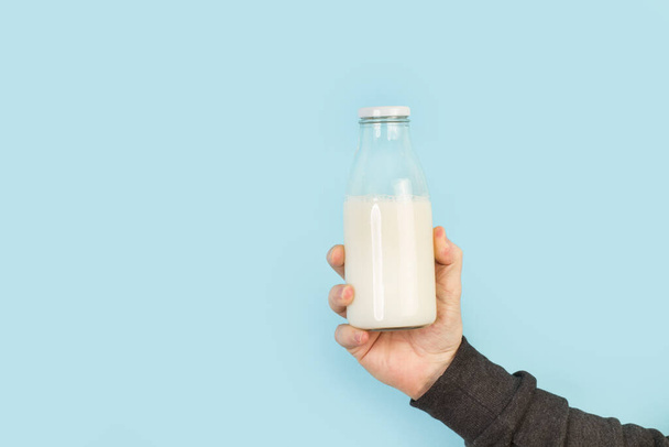 Mano de hombre sosteniendo una botella de leche sobre un fondo azul claro
 - Foto, Imagen
