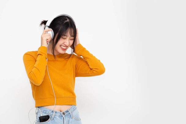 Beyaz arka planda izole edilmiş akıllı telefondaki müzik listesindeki kulaklıklarla müzik dinleyen genç Asyalı güzel kadın. - Fotoğraf, Görsel