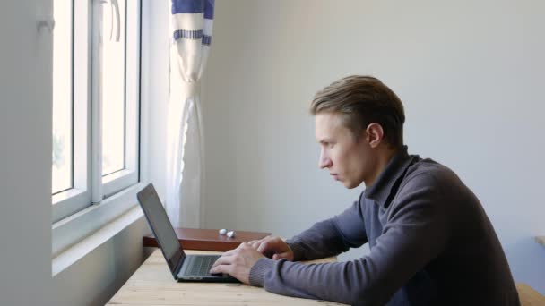 Genç adam dizüstü bilgisayar kullanıyor, daktilo ediyor, kaydırıyor, internette sörf yapıyor, ekrana bakıyor. Profesyonel yaratıcı milenyum, ofis stüdyosundaki masasında çalışıyor. Öğrenci çevrimiçi çalışıyor. 4k - Video, Çekim