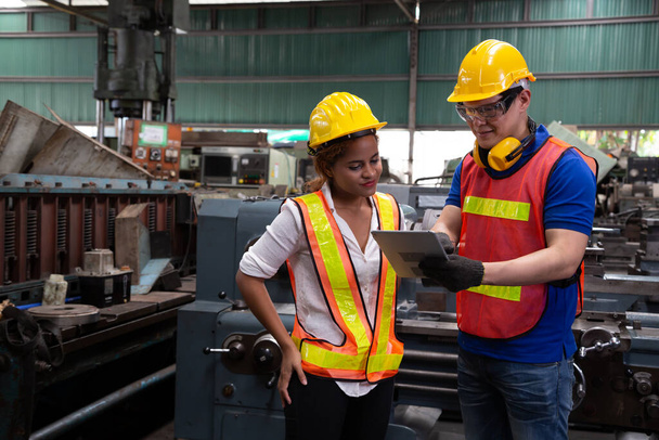 Engenheiro de fábrica vestindo chapéu amarelo e verificando a máquina e relatório de leitura por tablet, conceito de manutenção anual
 - Foto, Imagem