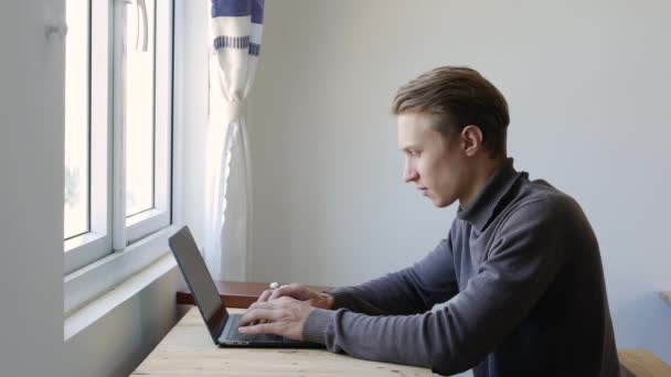 Młody człowiek freelancer za pomocą laptopa, pisanie na maszynie, przewijanie, surfing web, patrząc na ekranie. Profesjonalne, kreatywne tysiąclecie, pracujące przy jego biurku w pracowni biurowej. Student uczący się online. 4k - Materiał filmowy, wideo