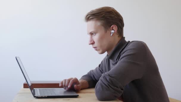 Νεαρός όμορφος άντρας χρησιμοποιεί φορητό υπολογιστή, κύλιση, σερφάρισμα στο διαδίκτυο, κοιτάζοντας την οθόνη. Επαγγελματική δημιουργική χιλιετηρίδα εργάζεται στο γραφείο του στο στούντιο γραφείο στο σπίτι. Φοιτητής που σπουδάζει online. 4ια - Πλάνα, βίντεο