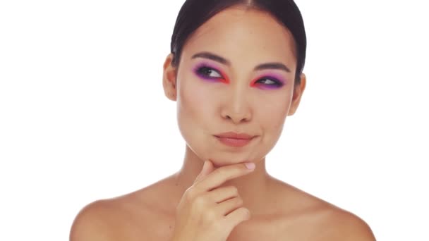 An attractive half-naked asian woman with bright fashion eye makeup is thinking about something and come up with an idea standing isolated over white background in studio. Gesturing with a finger - Metraje, vídeo