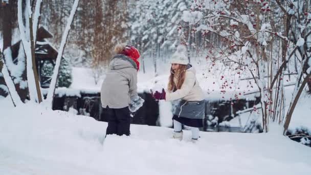 Happy children are playing with white snow together outdoors. Cheerful girls throw soft snow up over their heads in a beautiful forest in winter. Slow motion. - Materiał filmowy, wideo