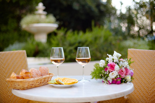 Pasteles frescos, platos de frutas, vasos con vino rosa y un ramo de hermosas flores sobre la mesa. Cena romántica en la terraza de la casa
 - Foto, imagen