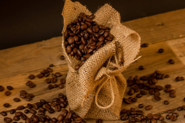 Жареный черный кофе в зернах, пролитый из джутового мешка в сырые доски
. - Фото, изображение