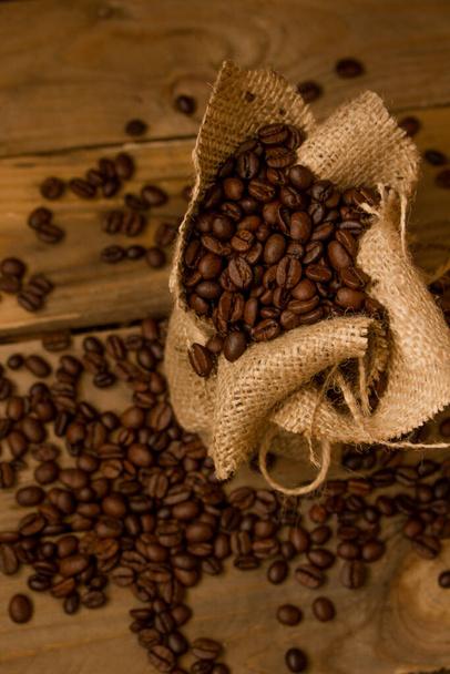 Жареный черный кофе в зернах, пролитый из джутового мешка в сырые доски
. - Фото, изображение
