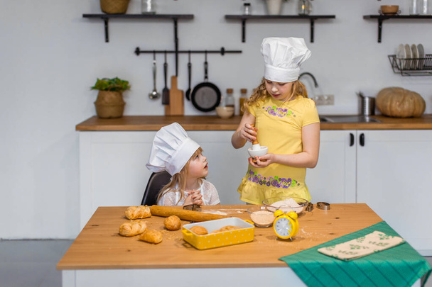 Family scene at home - two cute little sisters happily baking cookies and buns - Φωτογραφία, εικόνα