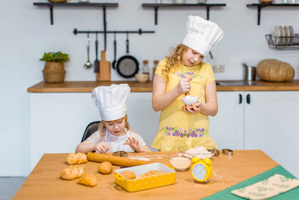 Family scene at home - two cute little sisters happily baking cookies and buns - Φωτογραφία, εικόνα