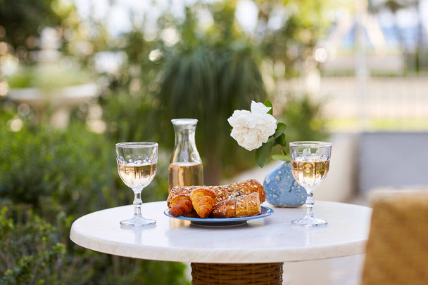 Zwei Gläser Wein und frisches Gebäck stehen auf dem Tisch. Romantisches Abendessen für zwei auf der Terrasse - Foto, Bild