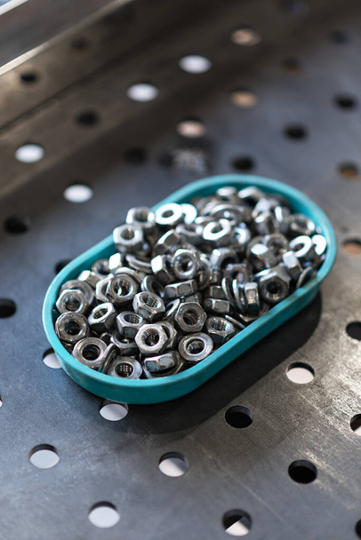 A handful of metal nuts in a plastic container for storage - Photo, Image