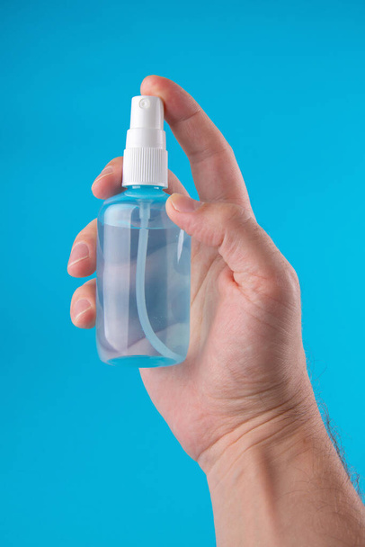 Coronavirus suojavarusteet - antiseptinen puhdistusaine spray. Miehen kädessä on pullo antiseptistä puhdistusainetta sinisellä pohjalla, lähikuva. Henkilökohtainen käsihygienia. Pullo desinfiointiainetta kädessä
. - Valokuva, kuva