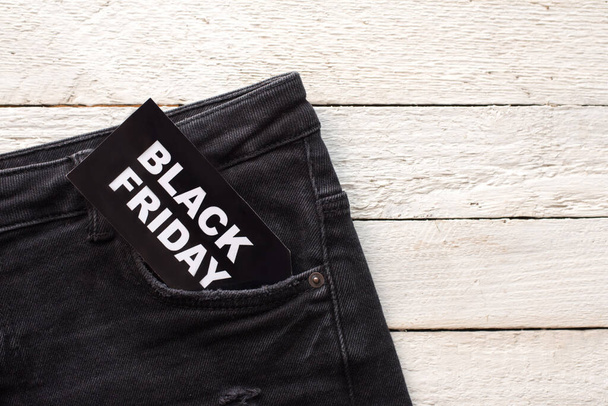 Jeans with black friday tag attached on white wood with copy space - Foto, Imagem