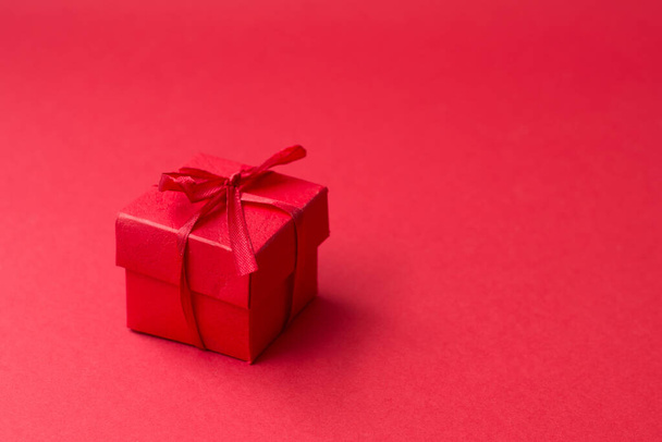 Kleines rotes Geschenk mit Schleife auf rotem Hintergrund. Freier Platz für Ihren Text. Grußkarte - Foto, Bild