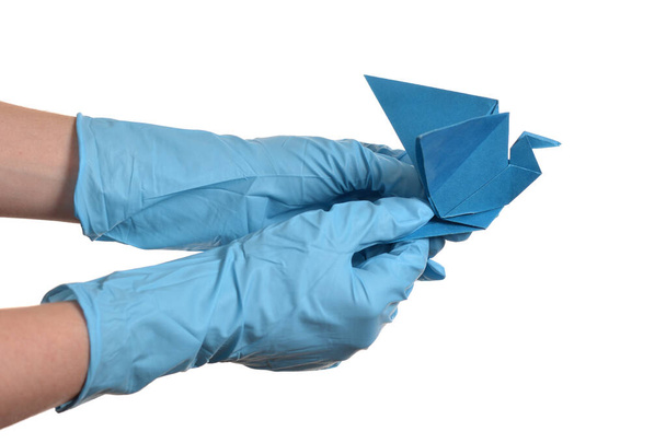 Орігамі паперовий кран в руці з гумовими рукавичками над білим
 - Фото, зображення
