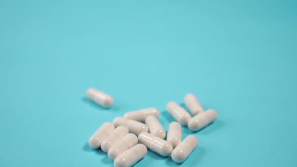 pile of white medical capsules on a blue bright table close-up. Slow camera down. Health concept - Video, Çekim