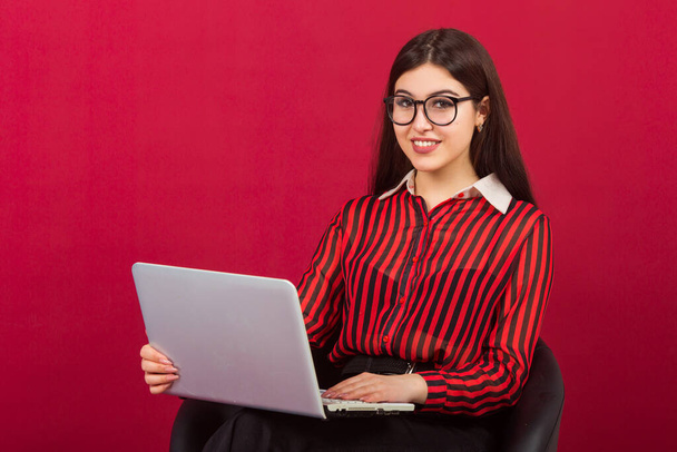beautiful young woman with make-up in a red suit on a red background with a laptop - Photo, Image