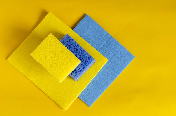 Yellow and blue kitchen sponges on top on a cleaning napkin. Bright kitchen utensils for cleaning close-up. The pleasure of cleaning. Selective focus. - Foto, afbeelding
