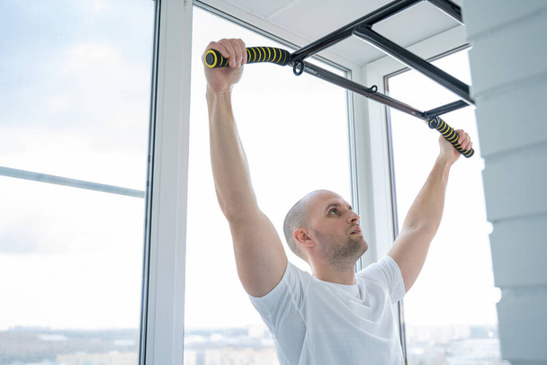 Man goes in for sports doing pull-up exercises on horizontal bar at his home - Фото, зображення