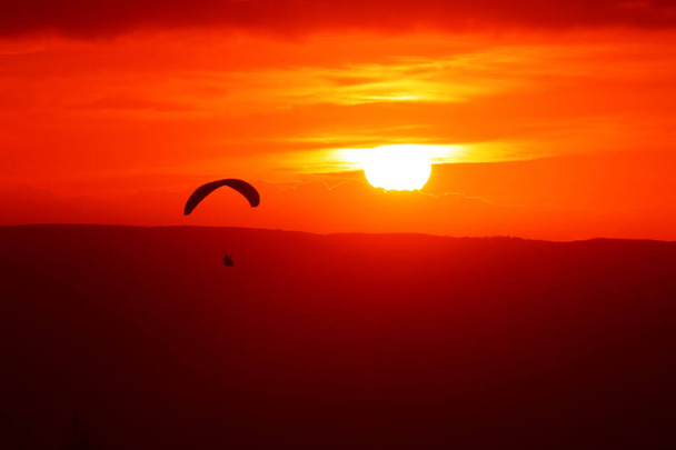 Paragliding at sunset.Beautiful red sunset with silhouette of a paraglider. - Фото, изображение