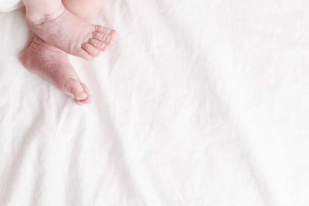 The legs of a newborn baby on a white bed top view - Foto, afbeelding