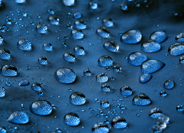 Regen waterdruppels op blauwe vezel waterdichte stof. Blauwe achtergrond. - Foto, afbeelding