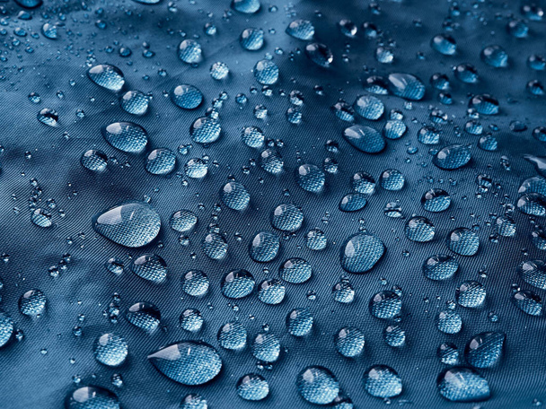 Σταγονίδια νερού βροχής σε αδιάβροχο ύφασμα μπλε ίνας. Μπλε φόντο. - Φωτογραφία, εικόνα