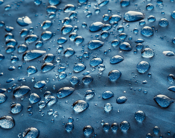 Капли дождевой воды на водонепроницаемой ткани из голубого волокна. Синий фон. - Фото, изображение