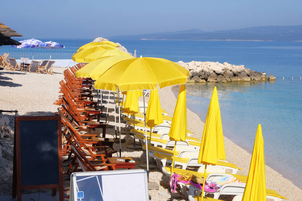 Strand sárga esernyők és szék pihenni és kényelmet a tengerparton. Boldog nyári vakációt és turisztikai koncepciót. Fizetett szolgáltatás vízparti strandokon. - Fotó, kép